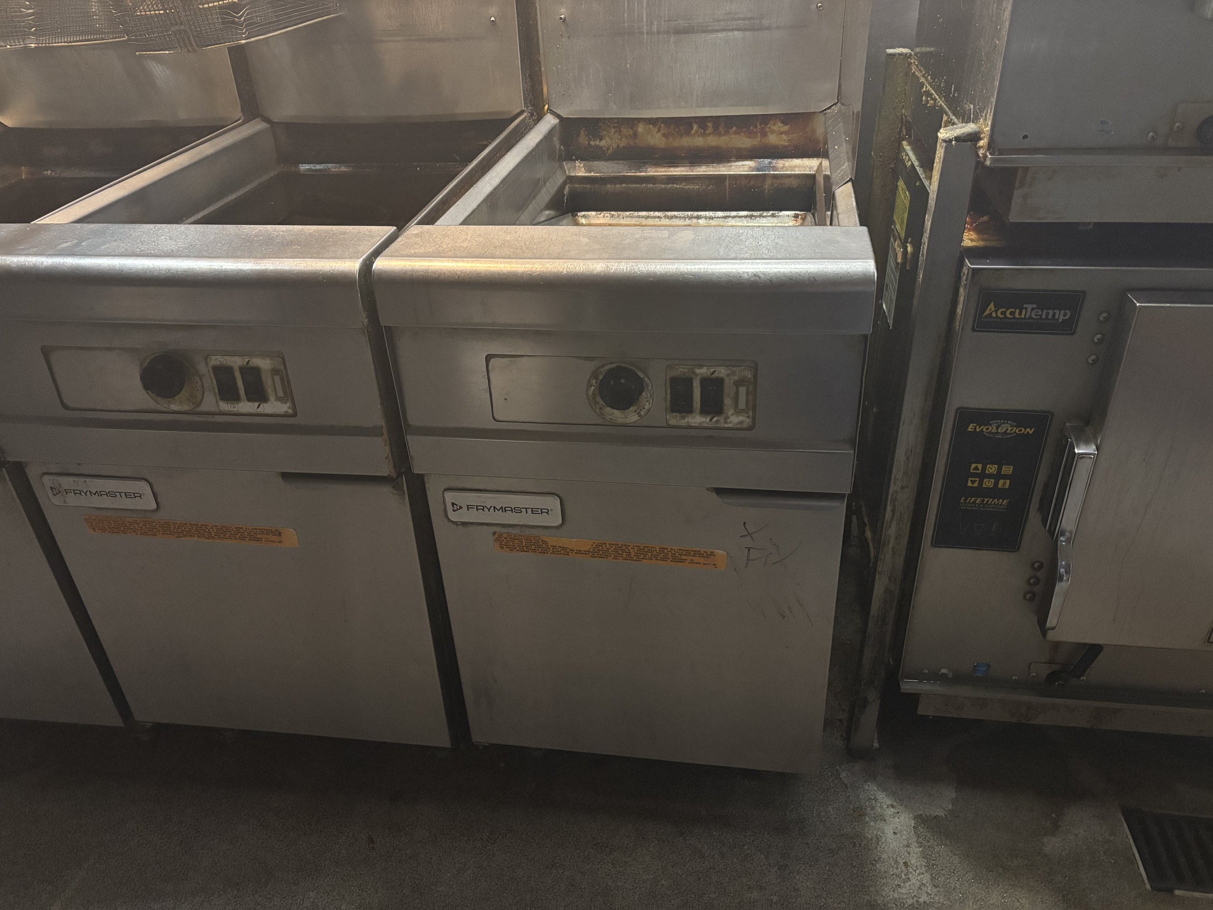 Commercial kitchen deep fryers labeled "Frymaster" next to an "AccuTemp" appliance.