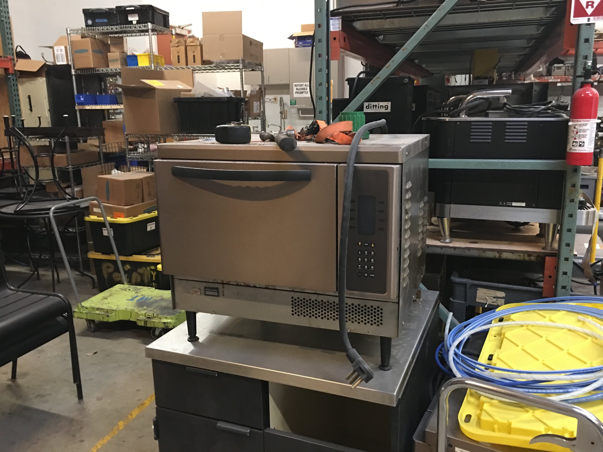 Commercial kitchen equipment and storage shelves in a warehouse with boxes and cables.