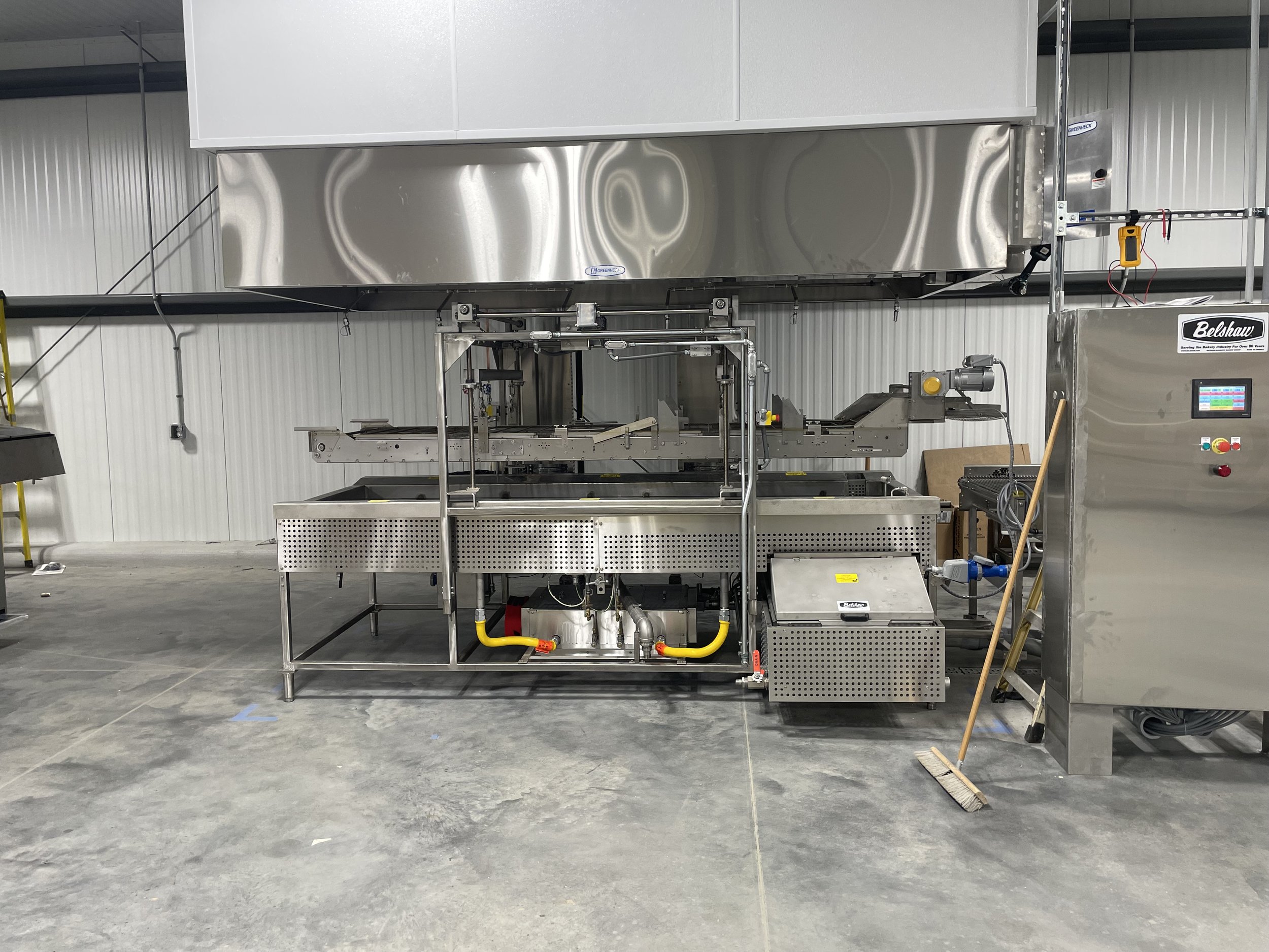 Industrial fryer machine in a factory setting with control panel, stainless steel design, and associated equipment.
