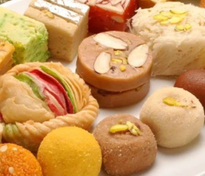 Assorted Indian sweets on a white plate, including ladoos, barfis, and halwa with nuts and pistachios on top.