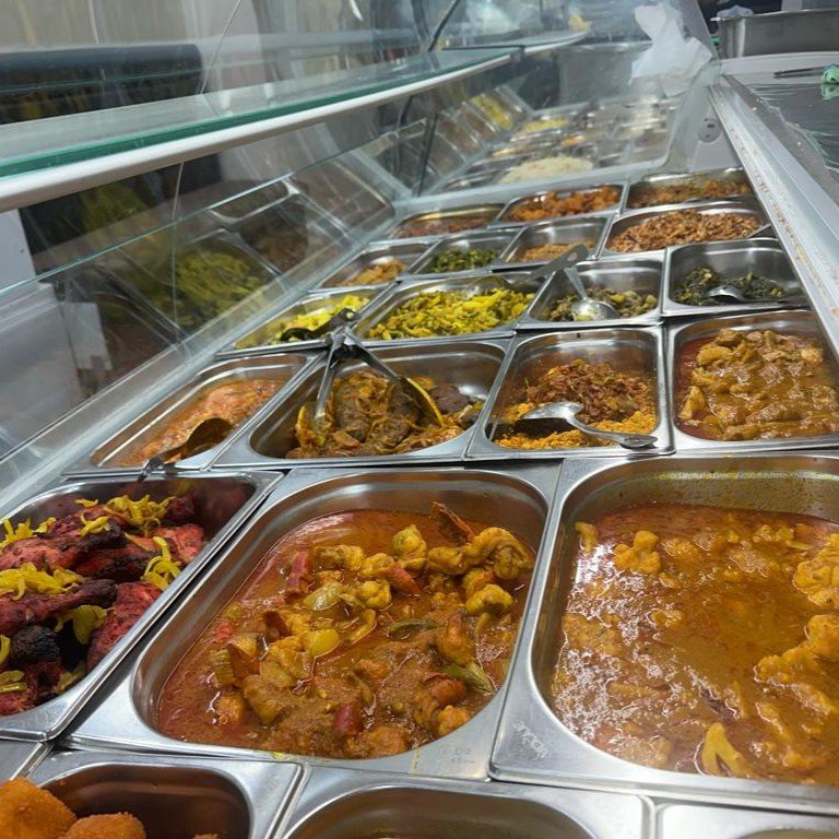 Buffet counter with various Indian dishes, including curries, kebabs, and vegetables in stainless steel trays.