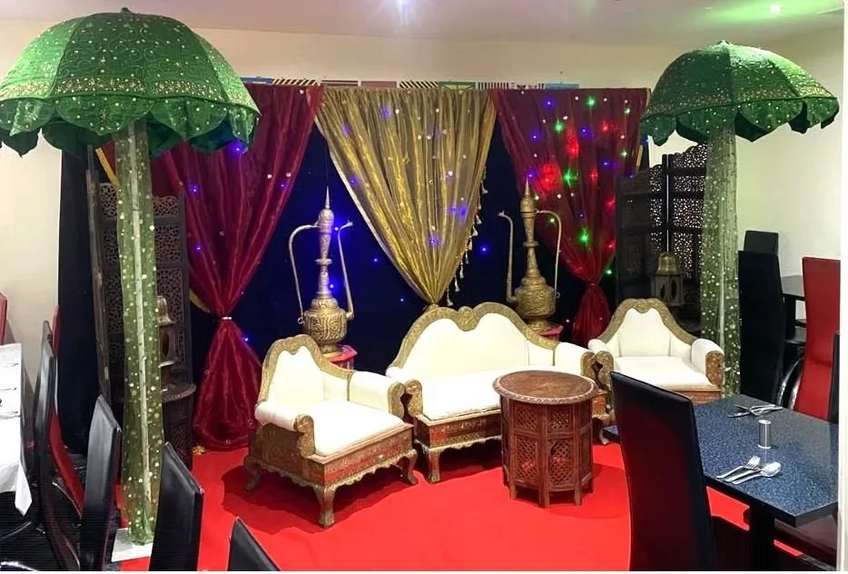 Luxurious seating area with ornate chairs, table, hookahs, and decorative drapes; indoor setting with green umbrellas and lights.