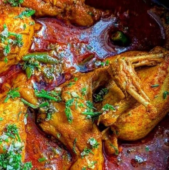 Spicy chicken curry garnished with fresh herbs, featuring pieces of chicken in a rich red sauce.