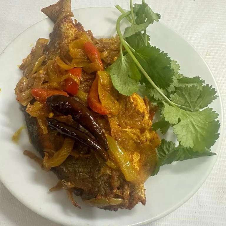 A cooked fish dish garnished with sliced peppers, chilies, and fresh cilantro on a white plate.