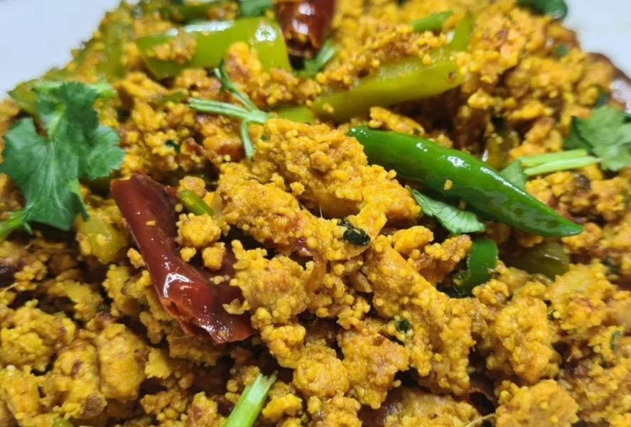 Close-up of a spiced scrambled egg dish with green chili peppers and cilantro garnish.