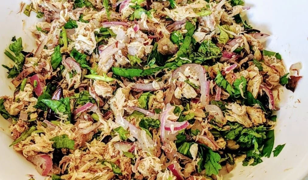 A bowl of shredded chicken salad with sliced red onions and fresh herbs.