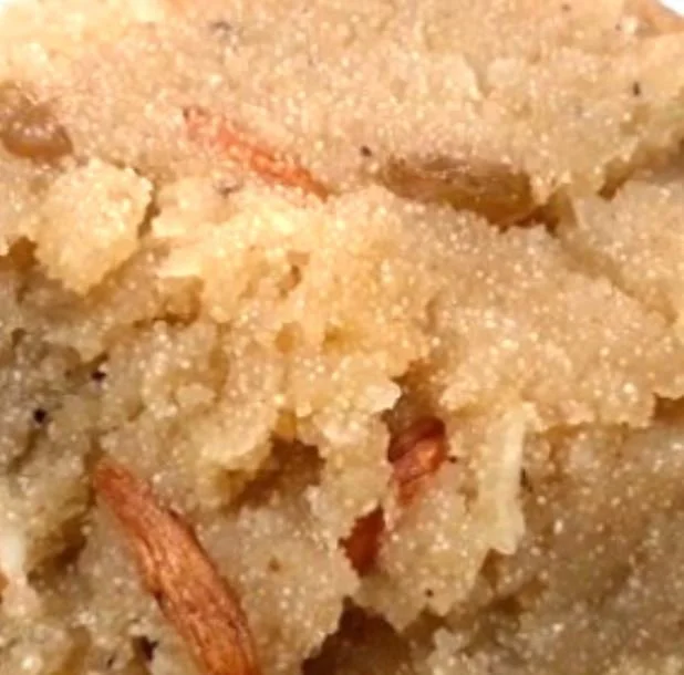 Close-up of Indian dessert, possibly suji ka halwa, with grains and nuts visible.