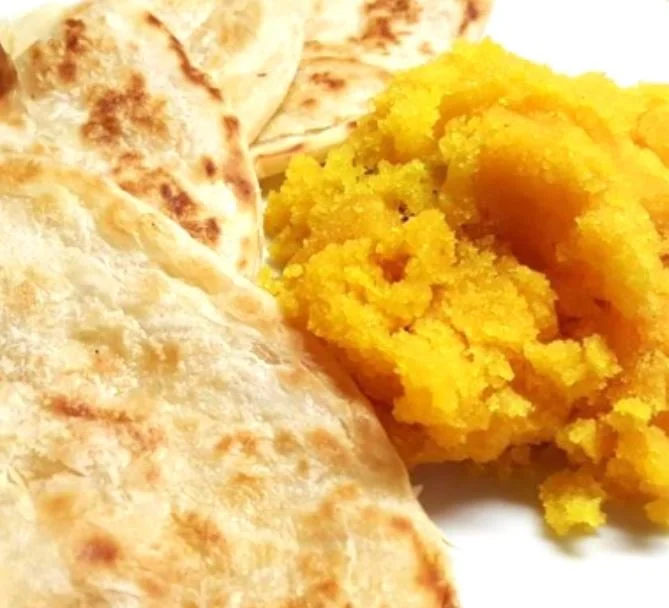 Close-up of flatbread and yellow-colored dish on a white plate.