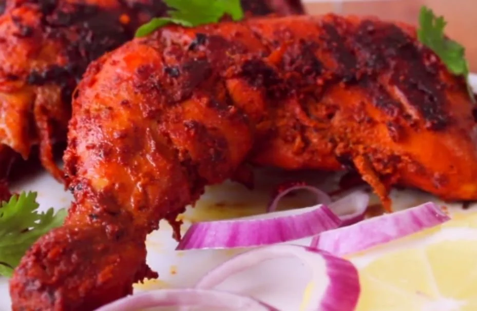 Spicy grilled chicken served with sliced red onions and lemon wedges.