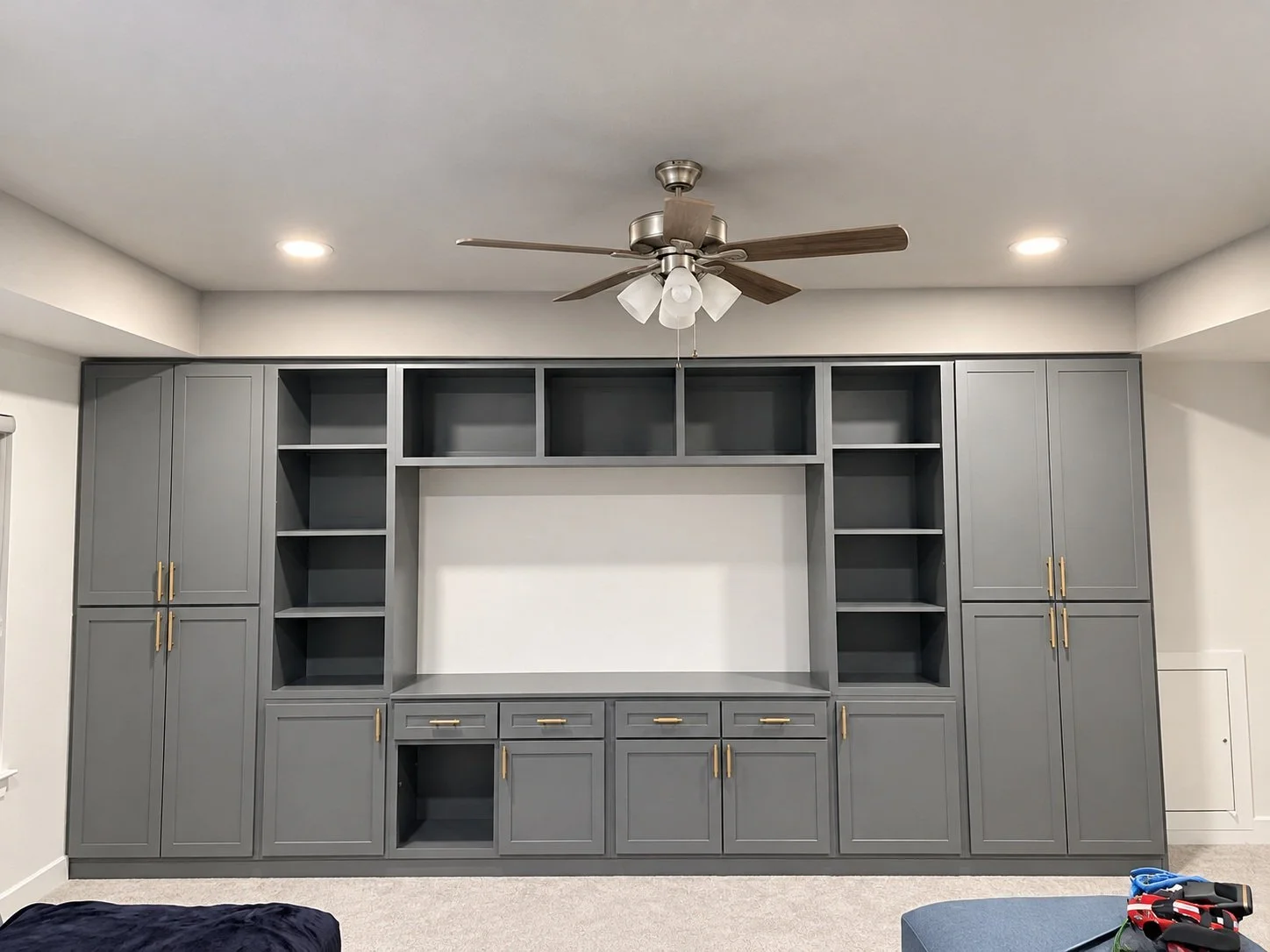 Gray wall storage with a central television niche, tall side cabinets, open shelves, and gold-tone hardware.