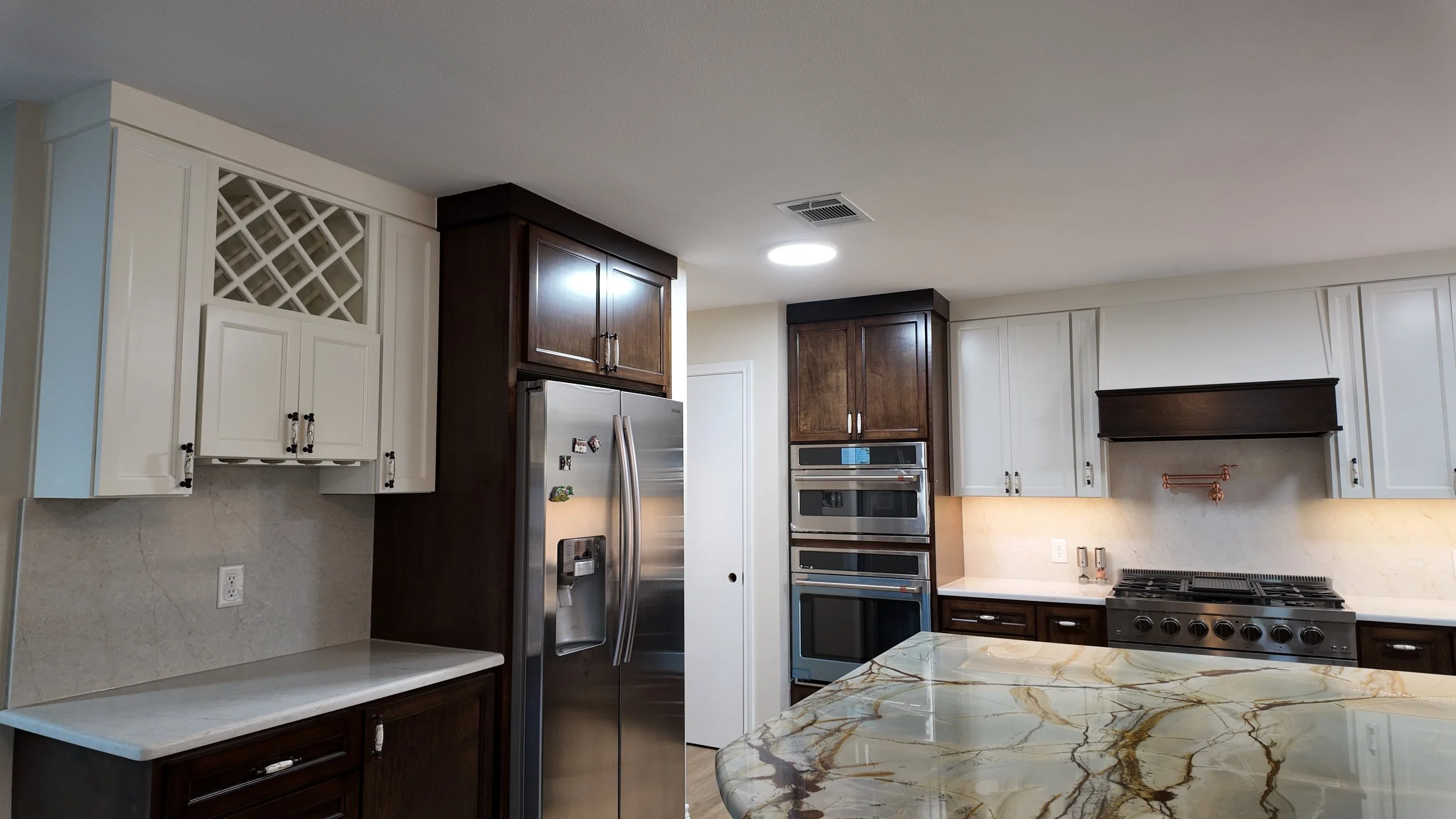 Modern kitchen with white and dark wood cabinets, stainless steel refrigerator, double oven, gas stove, and a marble countertop island.