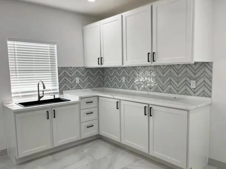 Modern kitchen with white cabinets, a black sink, a window with blinds, and a gray herringbone tile backsplash.