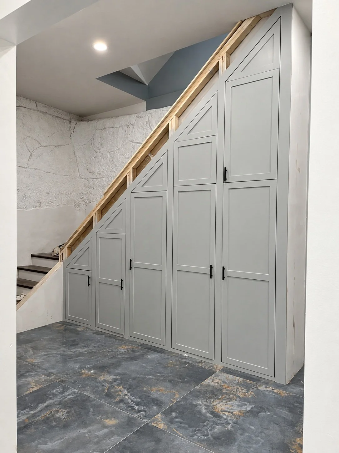 Gray cabinet doors follow the angle beneath a staircase, with slim black handles and a tailored fit.