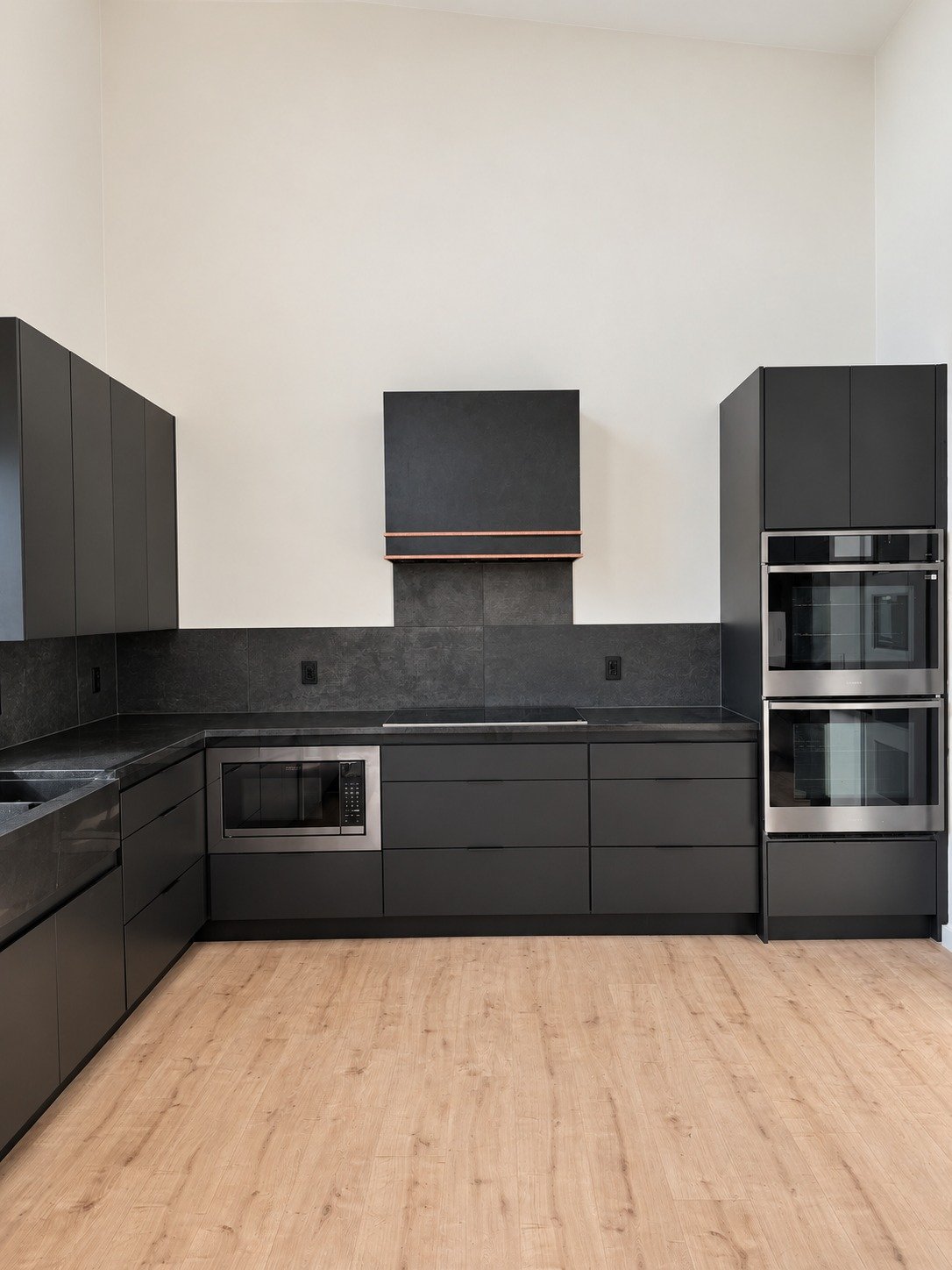A wide view of the cabinetry, appliances, and dark range hood.
