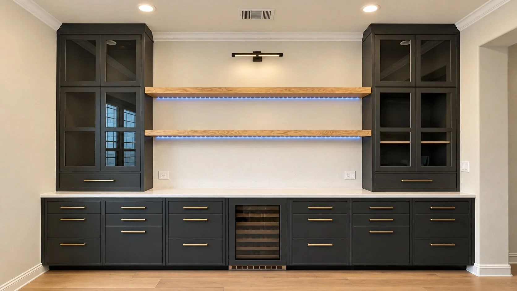Dark bar cabinetry with glass-front doors, warm wood floating shelves, accent lighting, gold-tone pulls, and a built-in beverage cooler.
