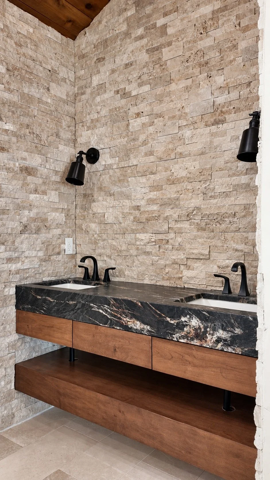 Custom wood double vanity with dark stone countertop, black faucets and a textured stone wall.