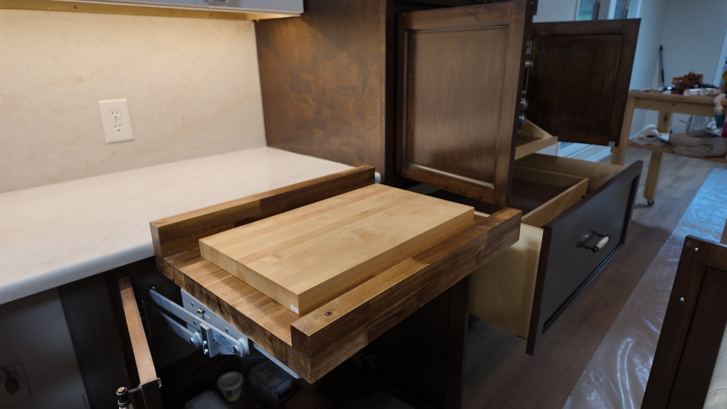 Disassembled kitchen cabinets and countertop with a cutting board, in a kitchen with ongoing renovation.