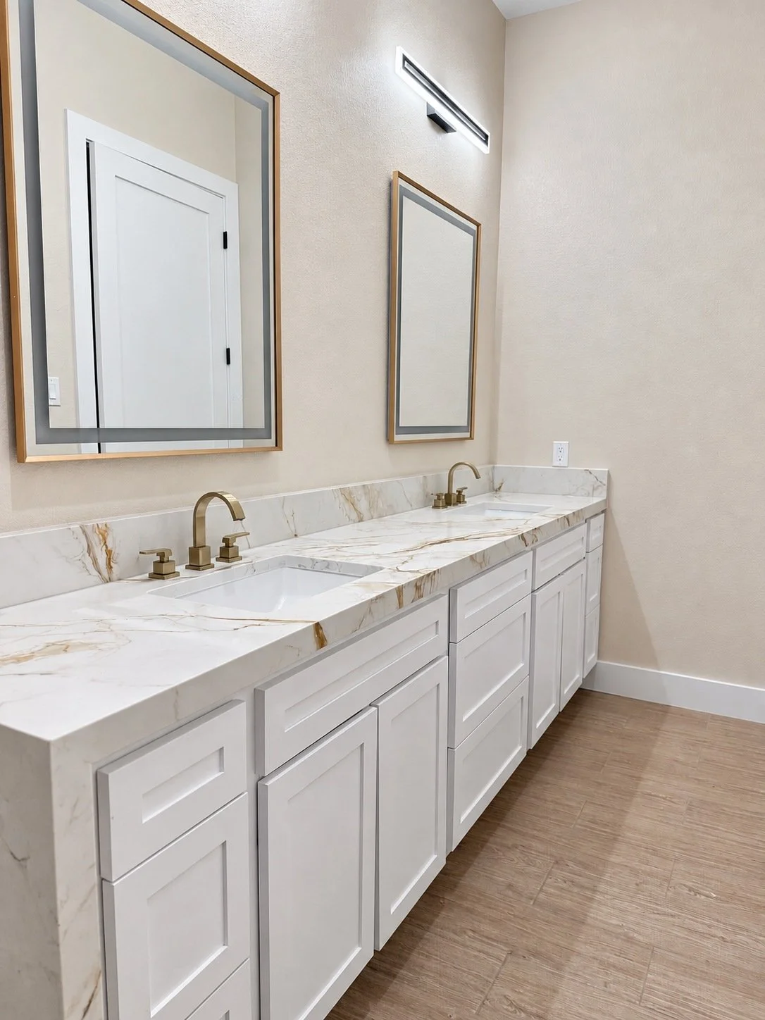 White double vanity with gold-tone faucets, two framed mirrors, and a light countertop with warm veining.