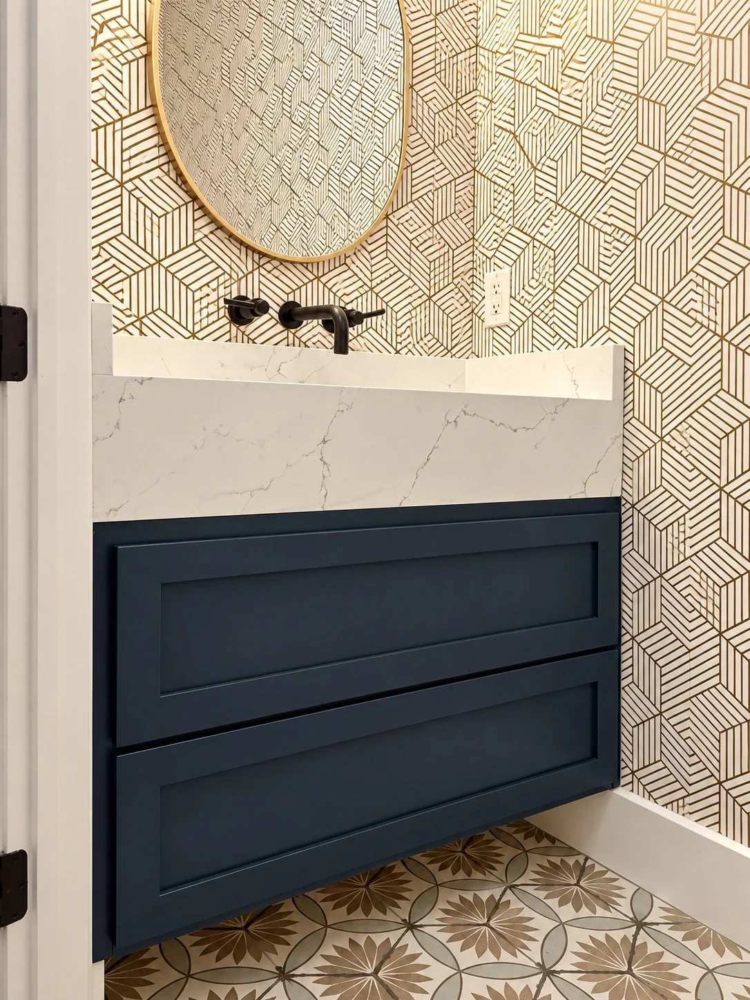 Dark floating vanity with a pale veined basin, black wall-mounted faucet, rounded mirror, and geometric patterned wallpaper.
