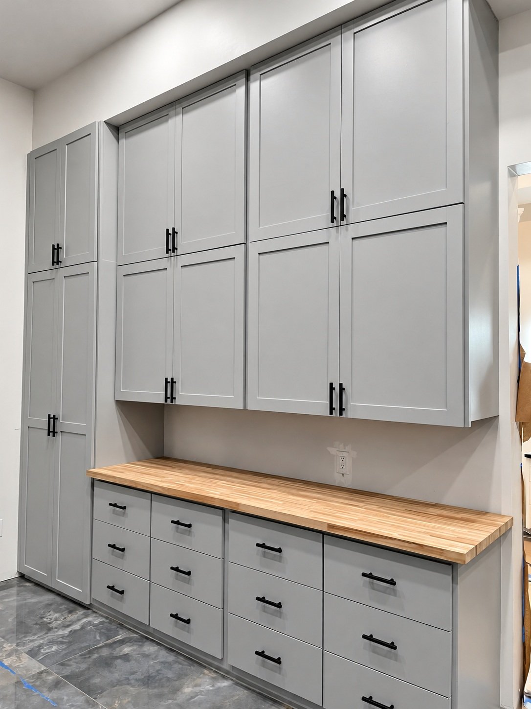 Gray cabinetry with black pulls, full-height storage, and a warm wood work surface above organized drawer banks.
