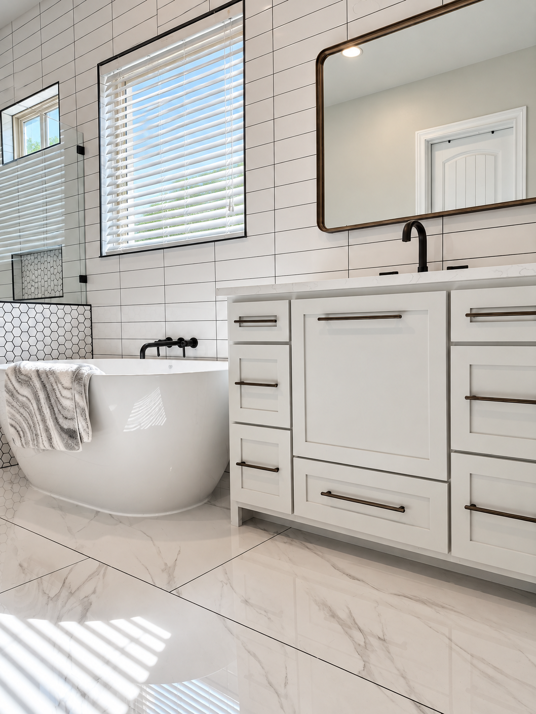 Full custom bathroom remodel with white cabinetry, dark fixtures, freestanding tub and marble-look tile.