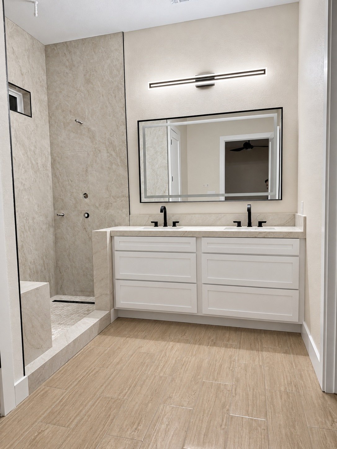 White double vanity with black faucets, a wide framed mirror, and a light countertop beside the shower area.