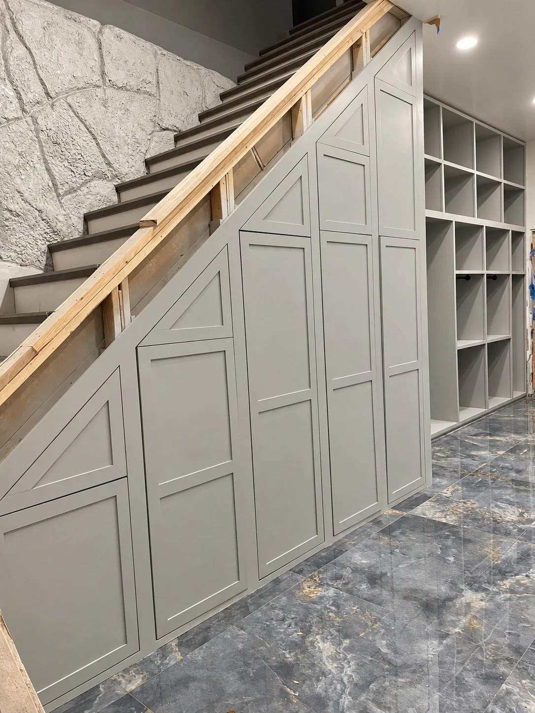 Angled under-stair cabinetry and adjacent open shelving make use of a compact storage area.