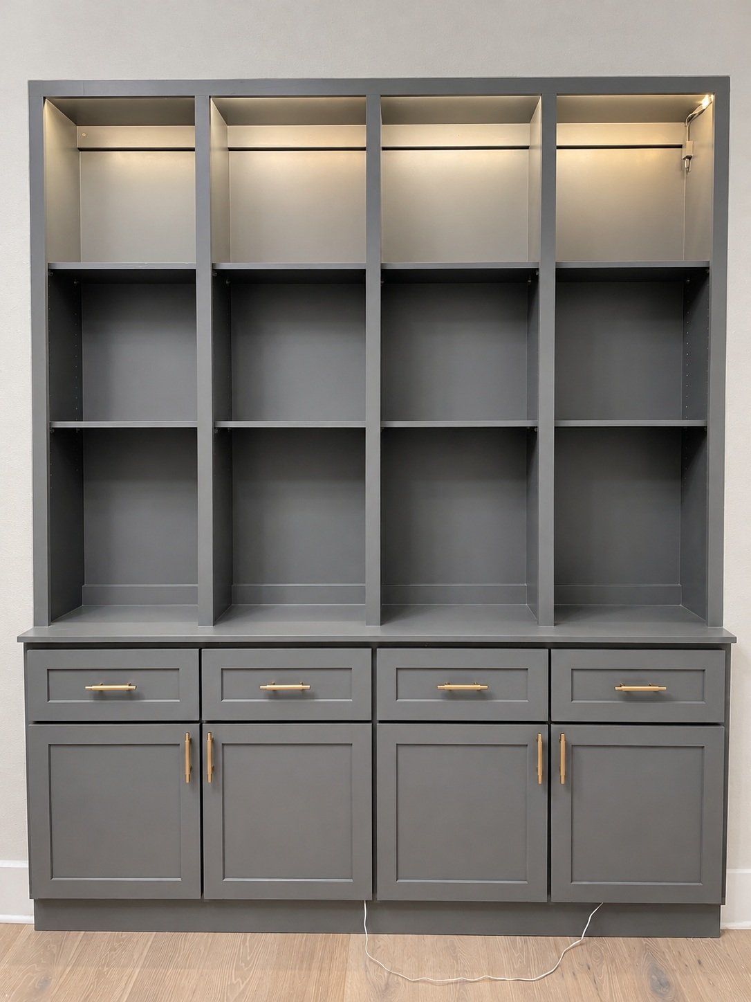 Four tall gray shelving bays with illuminated upper compartments, lower drawers, cabinet doors, and gold-tone pulls.