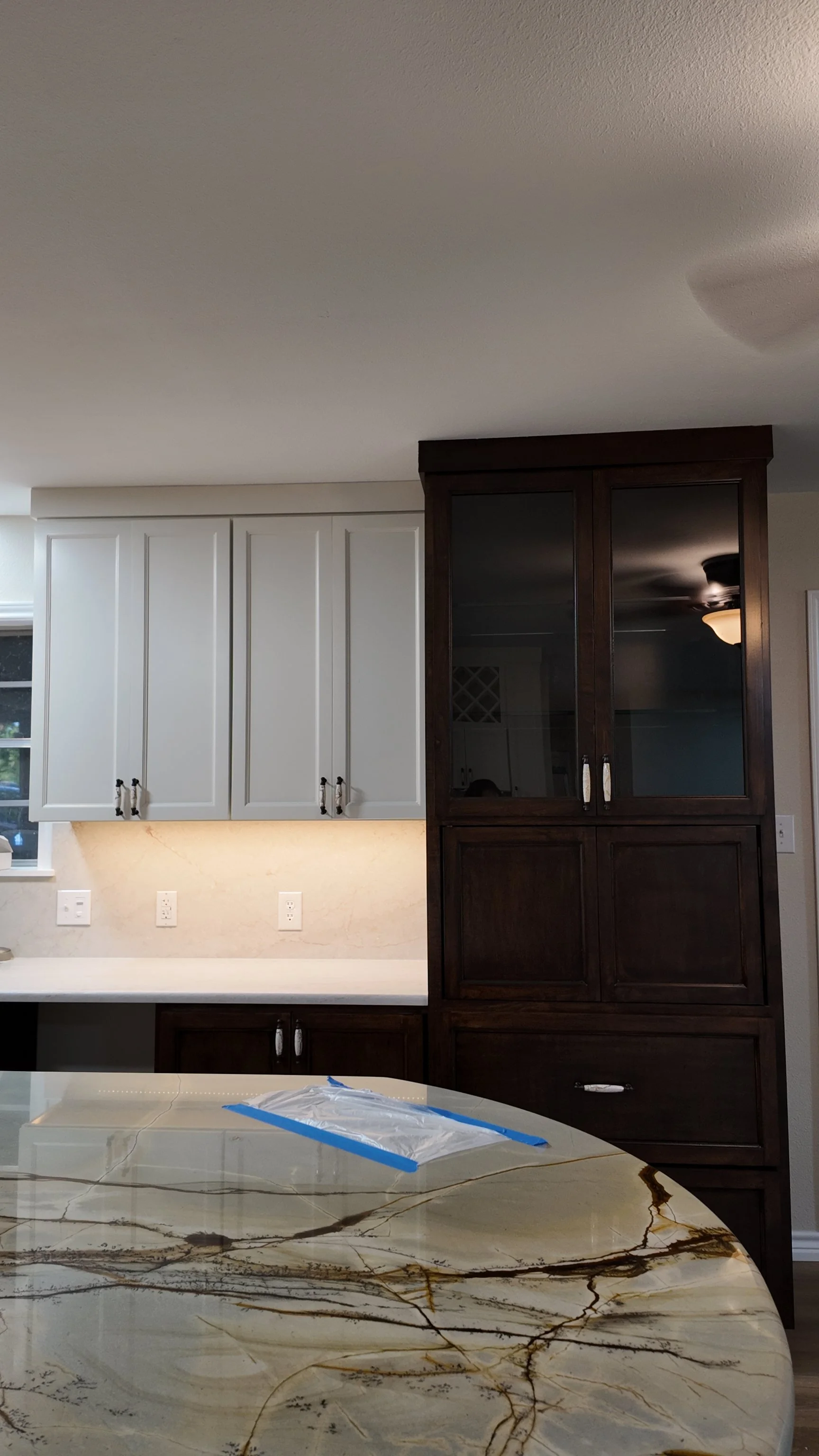 A kitchen with white upper cabinets, dark wood lower cabinets, and a marble countertop with brown and beige veining.