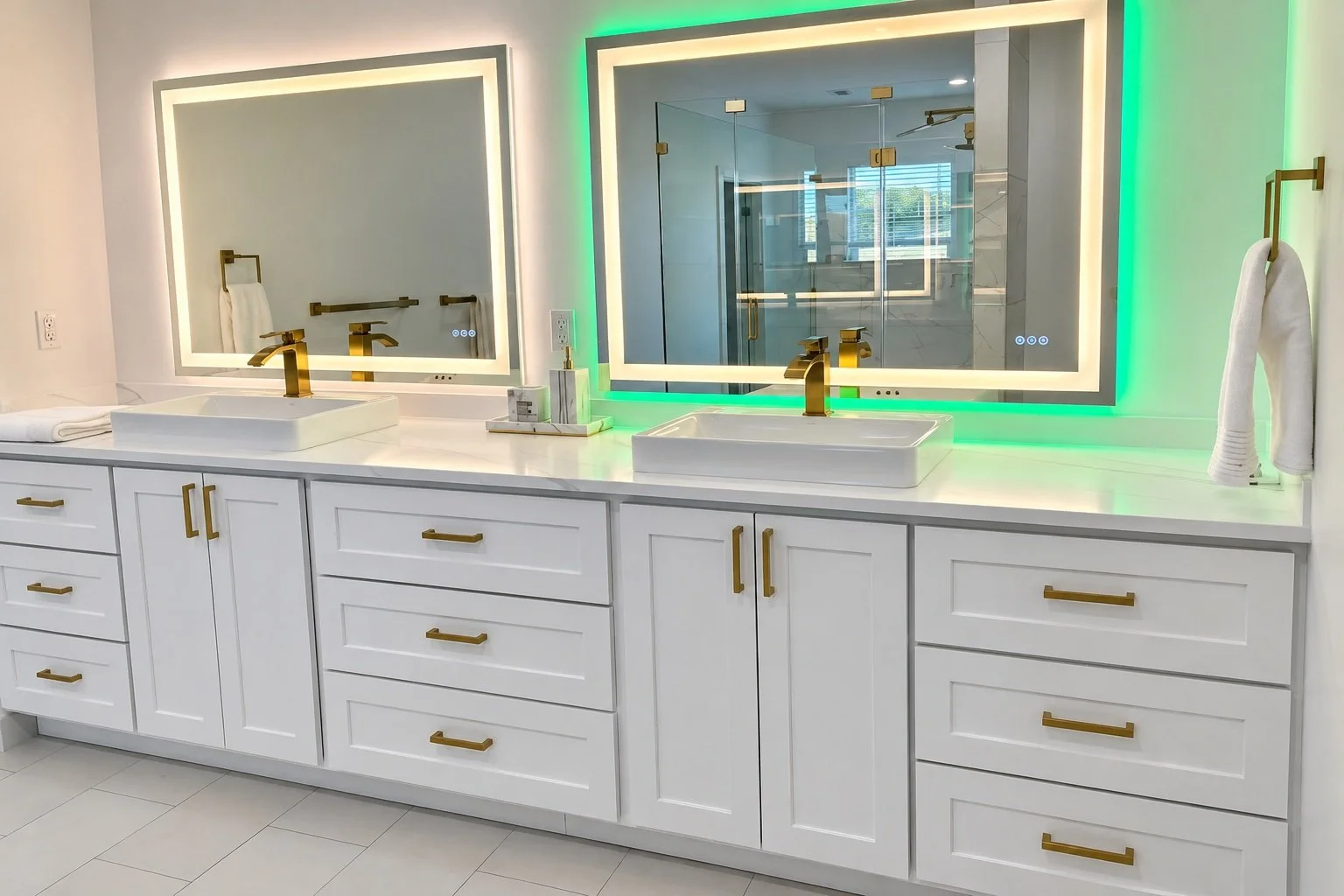 White double vanity with gold-tone hardware, two vessel sinks, and illuminated mirrors with green accent lighting.