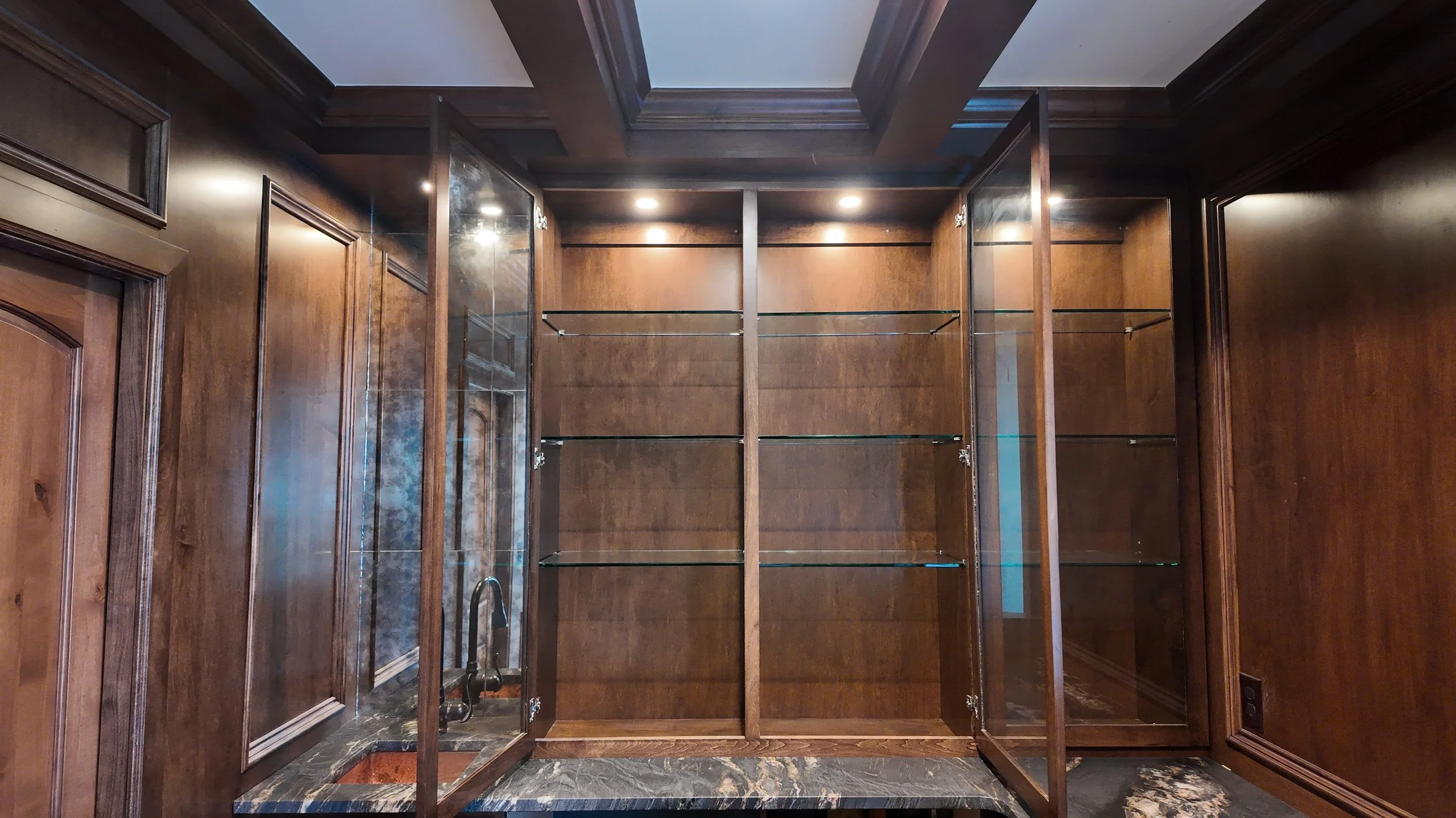 Empty wooden display cabinet with glass shelves and doors in a wood-paneled room.