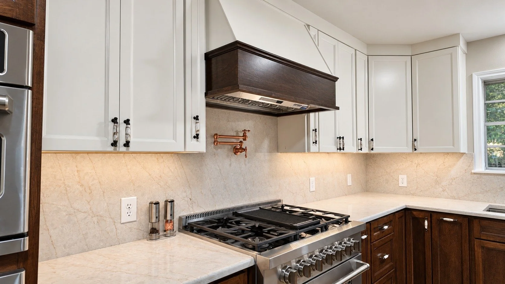 Dark range hood, light cabinetry, and a brass pot filler.