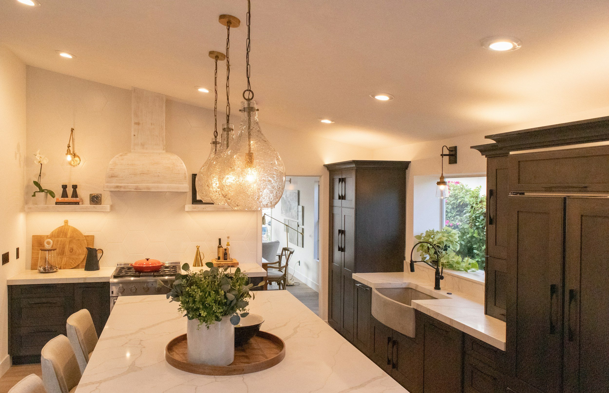 Modern kitchen with beige and dark wood cabinets, white countertops, large hanging light fixtures, and farmhouse sink.