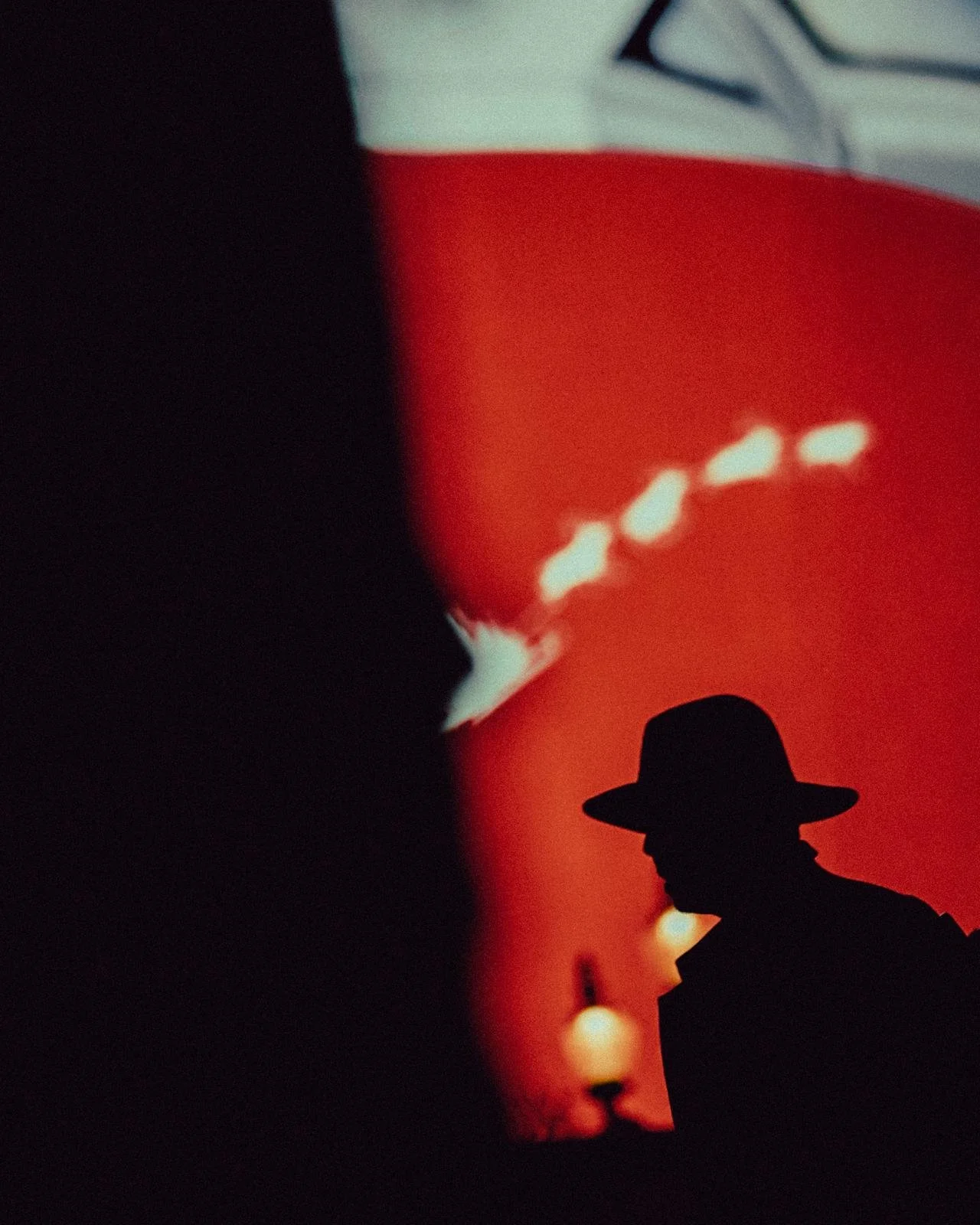 Silhouette of a man wearing a wide-brimmed hat against a red and black background with blurred lights.