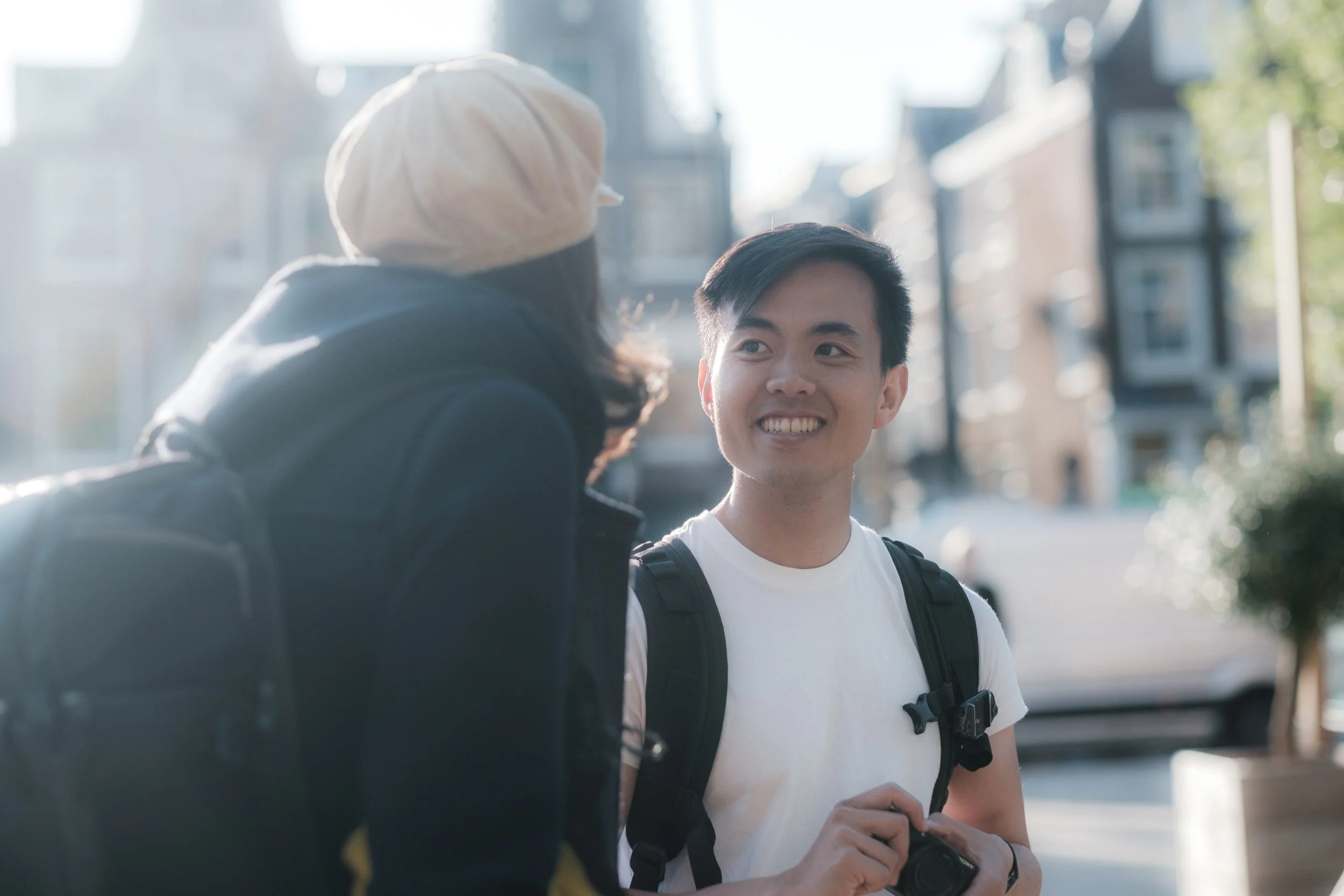 Two young people with backpacks talking outdoors in an urban setting, smiling and engaging with each other.