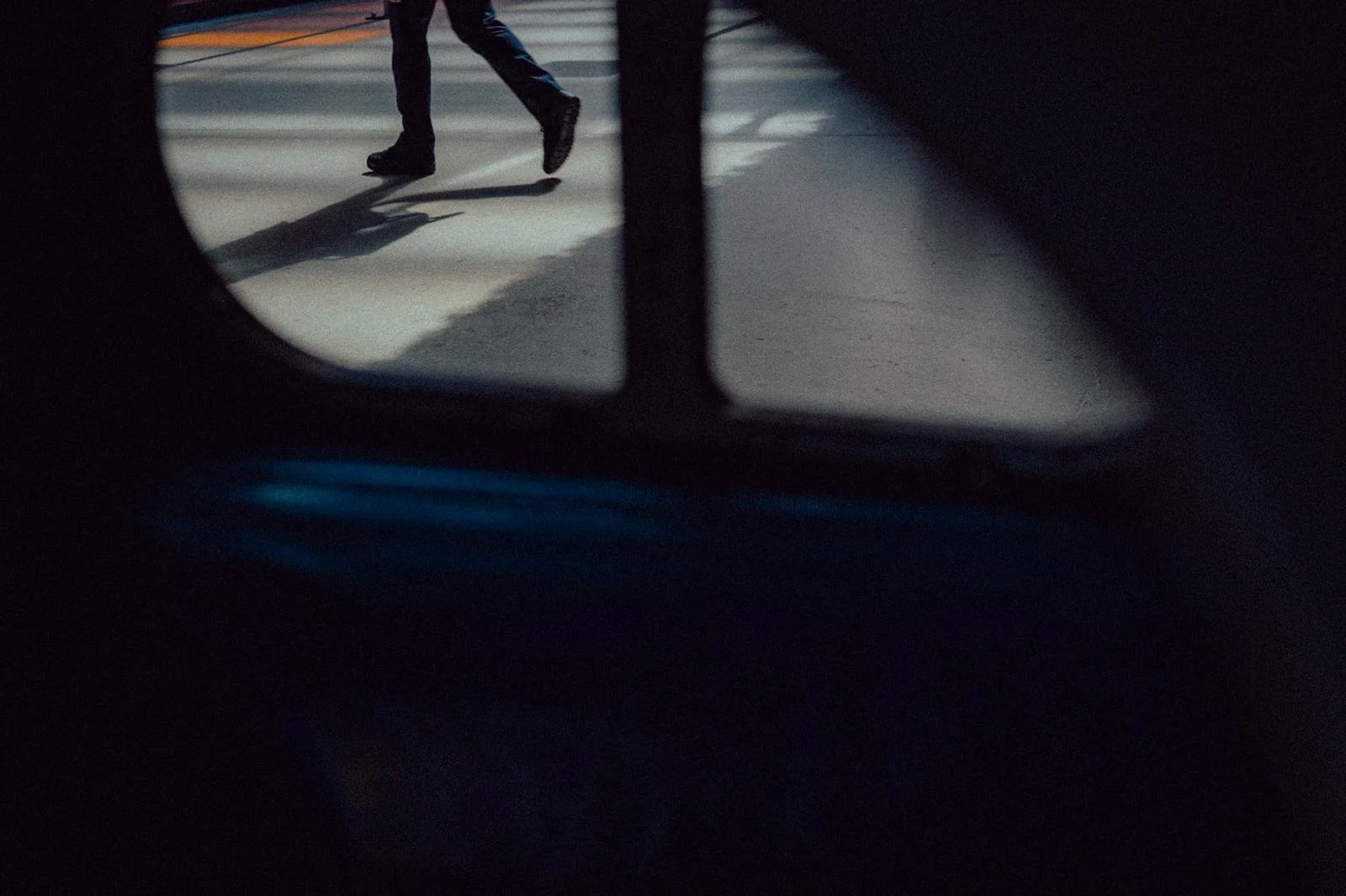Person walking on a parking lot, viewed through a hole or window with darkness around the edges.