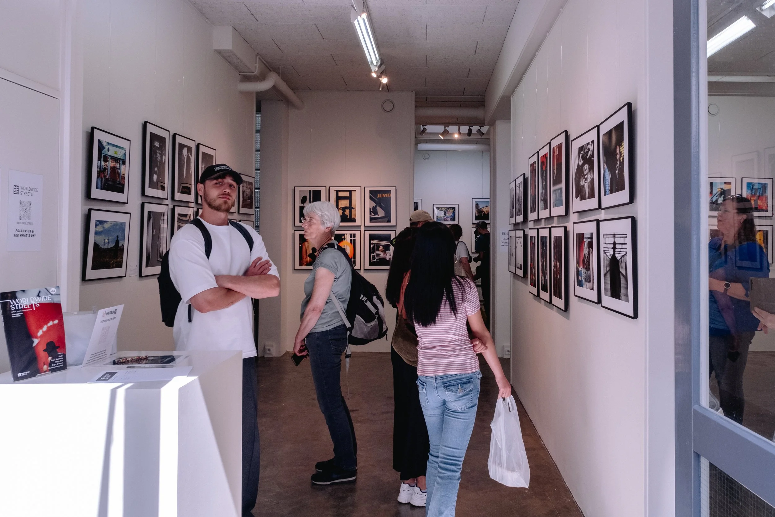 People viewing framed photographs in an art gallery with white walls and wooden floors.