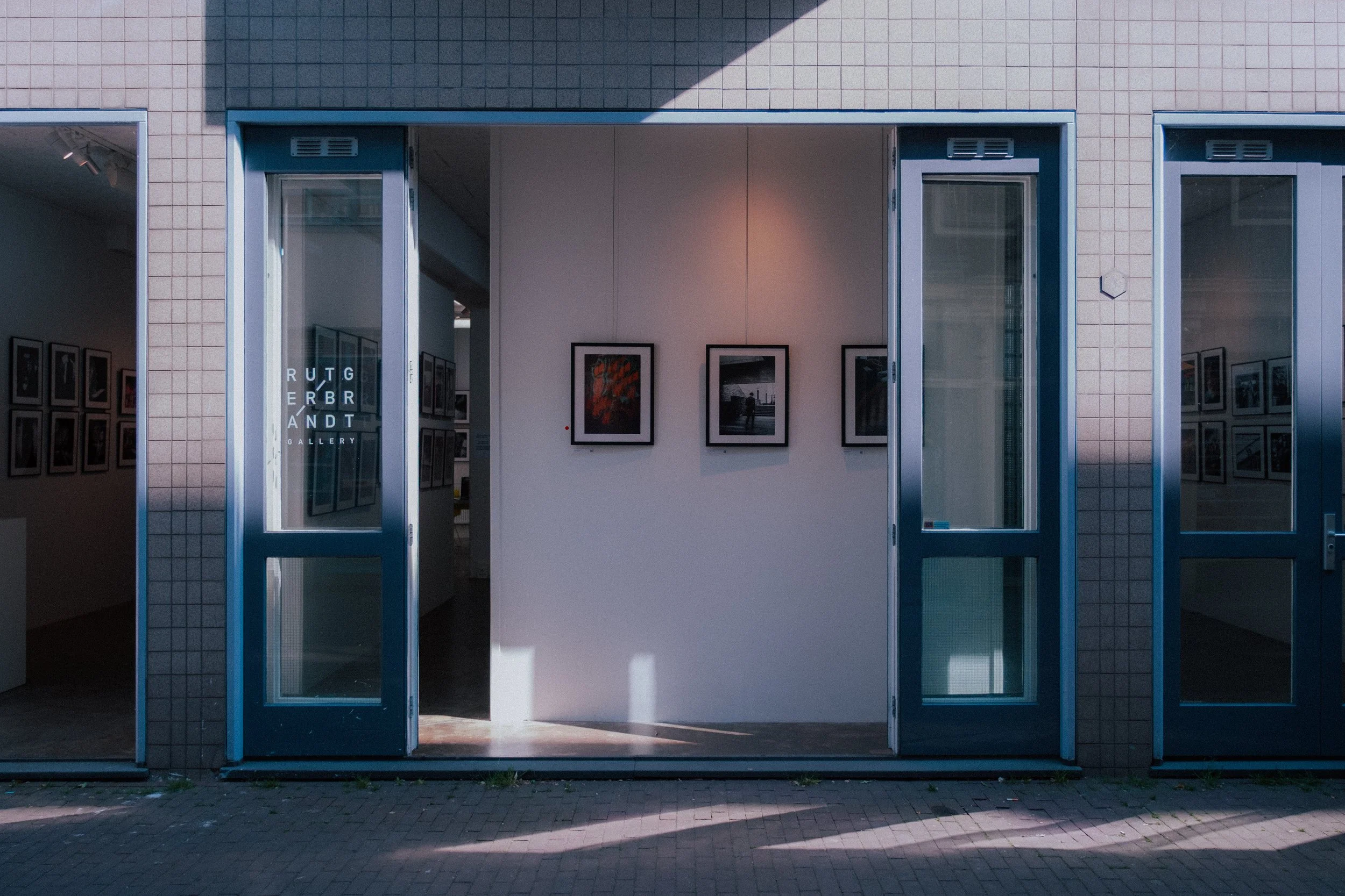 Open doors of an art gallery with framed photographs on white walls visible inside and a sign on the glass door reading "RUTGER BRANDT GALLERY."