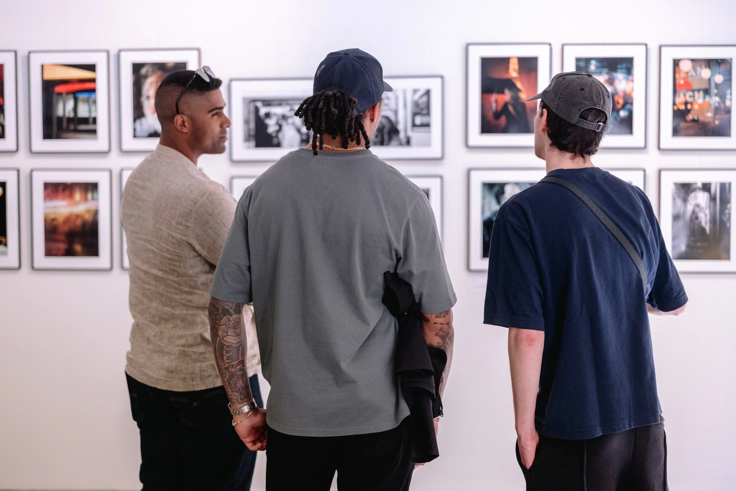 Three men looking at framed photographs on a gallery wall.