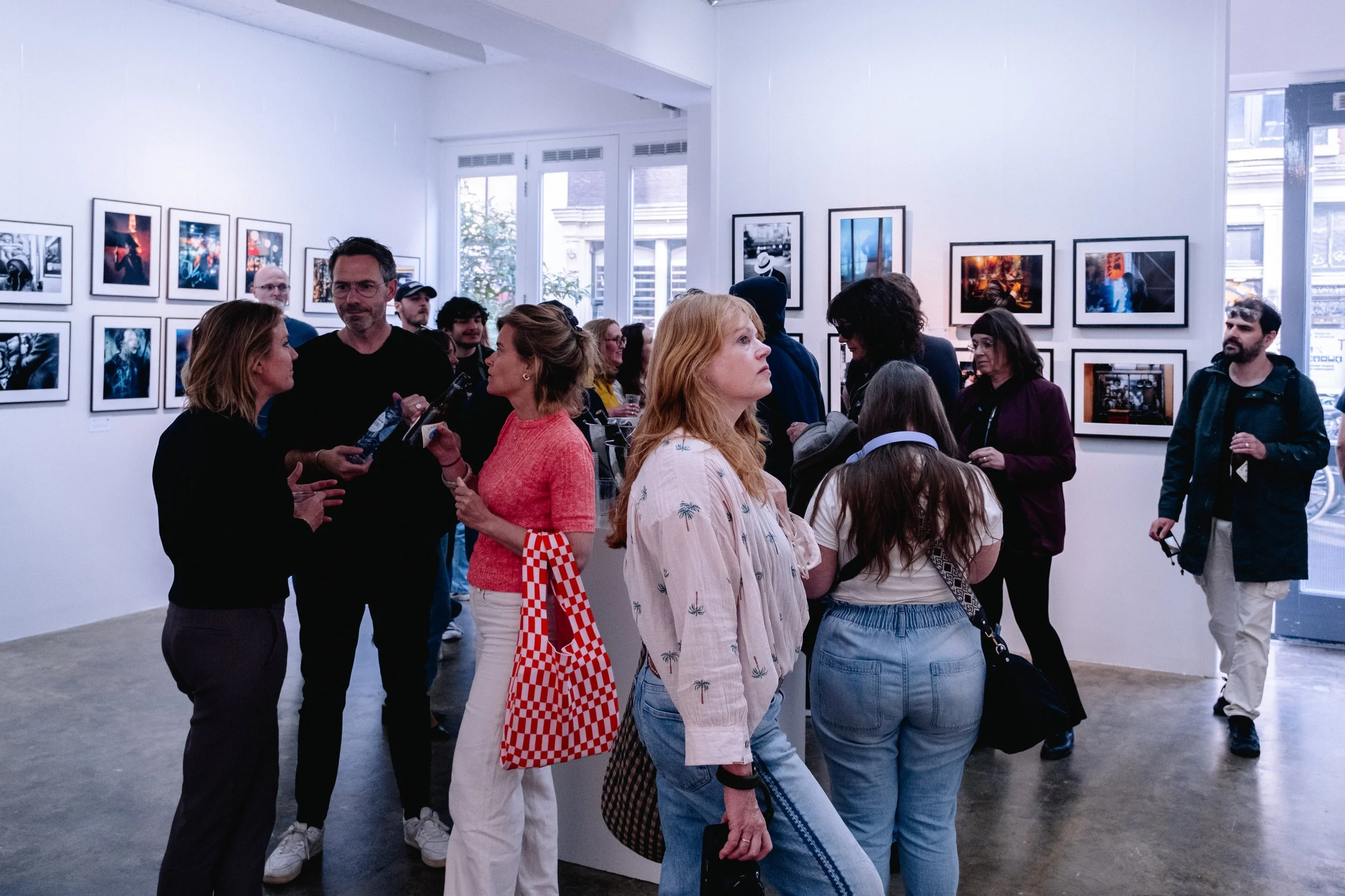 People viewing and discussing photographs in an art gallery with white walls and framed pictures displayed on the walls.