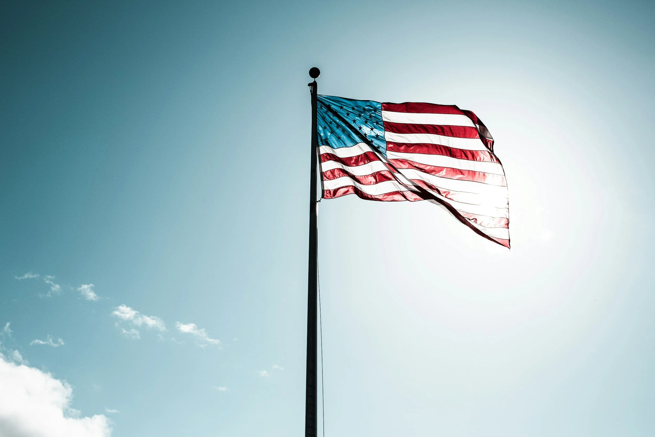 American flag waving against a blue sky with some clouds.