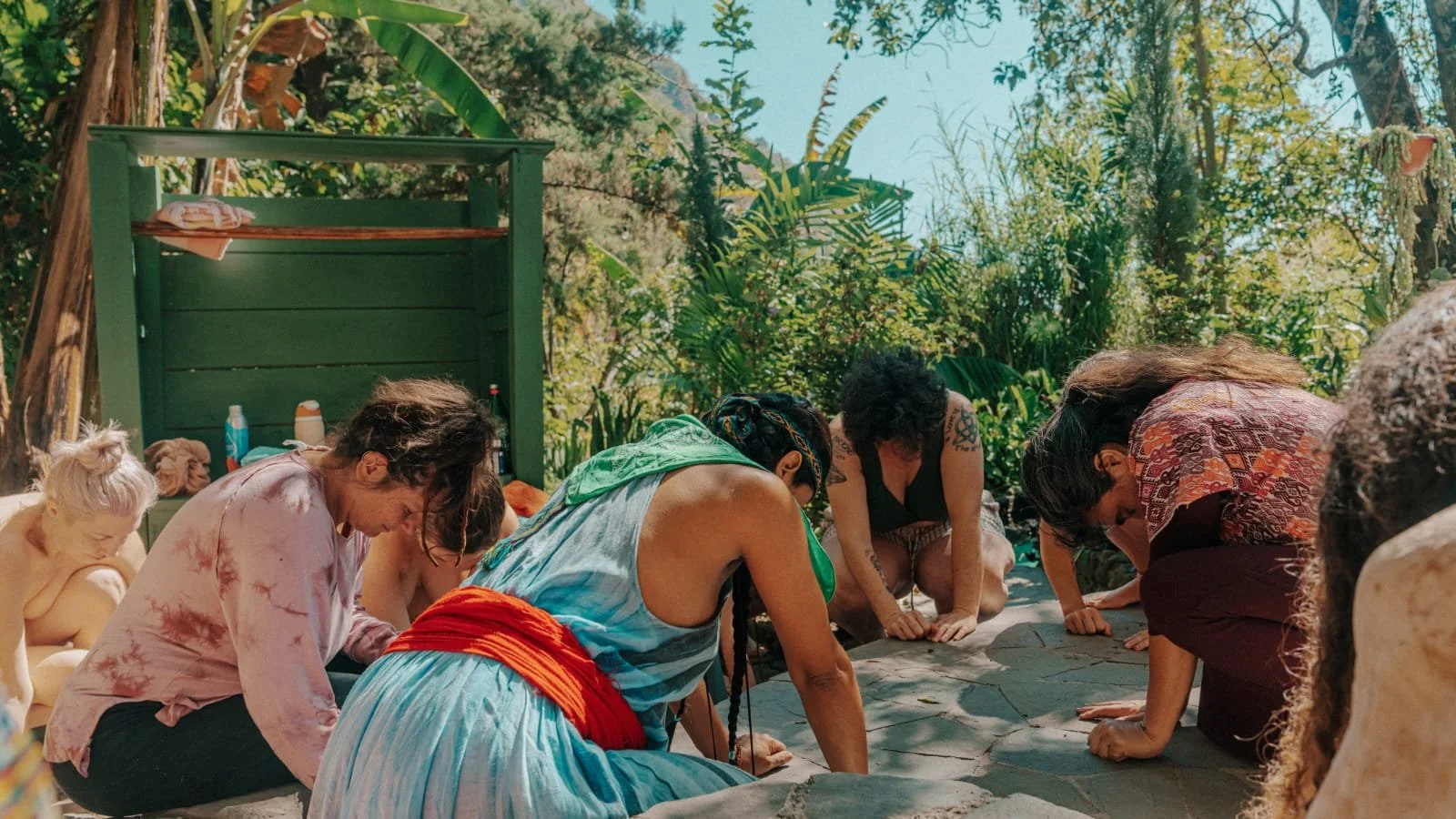 People practicing yoga or meditation outdoors in a lush, green setting with trees and plants.
