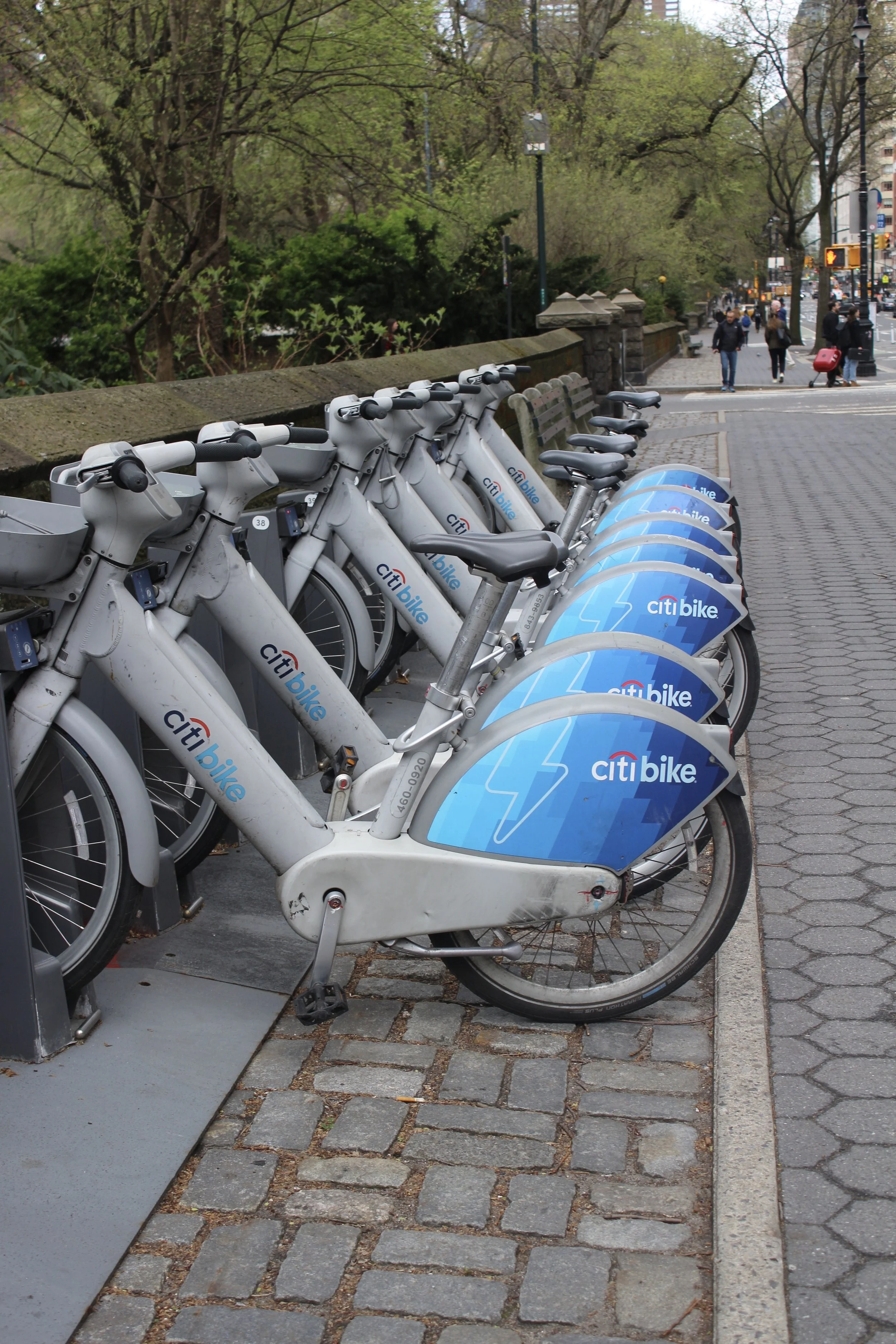 Row of Citi Bikes parked at a docking station on a city sidewalk.