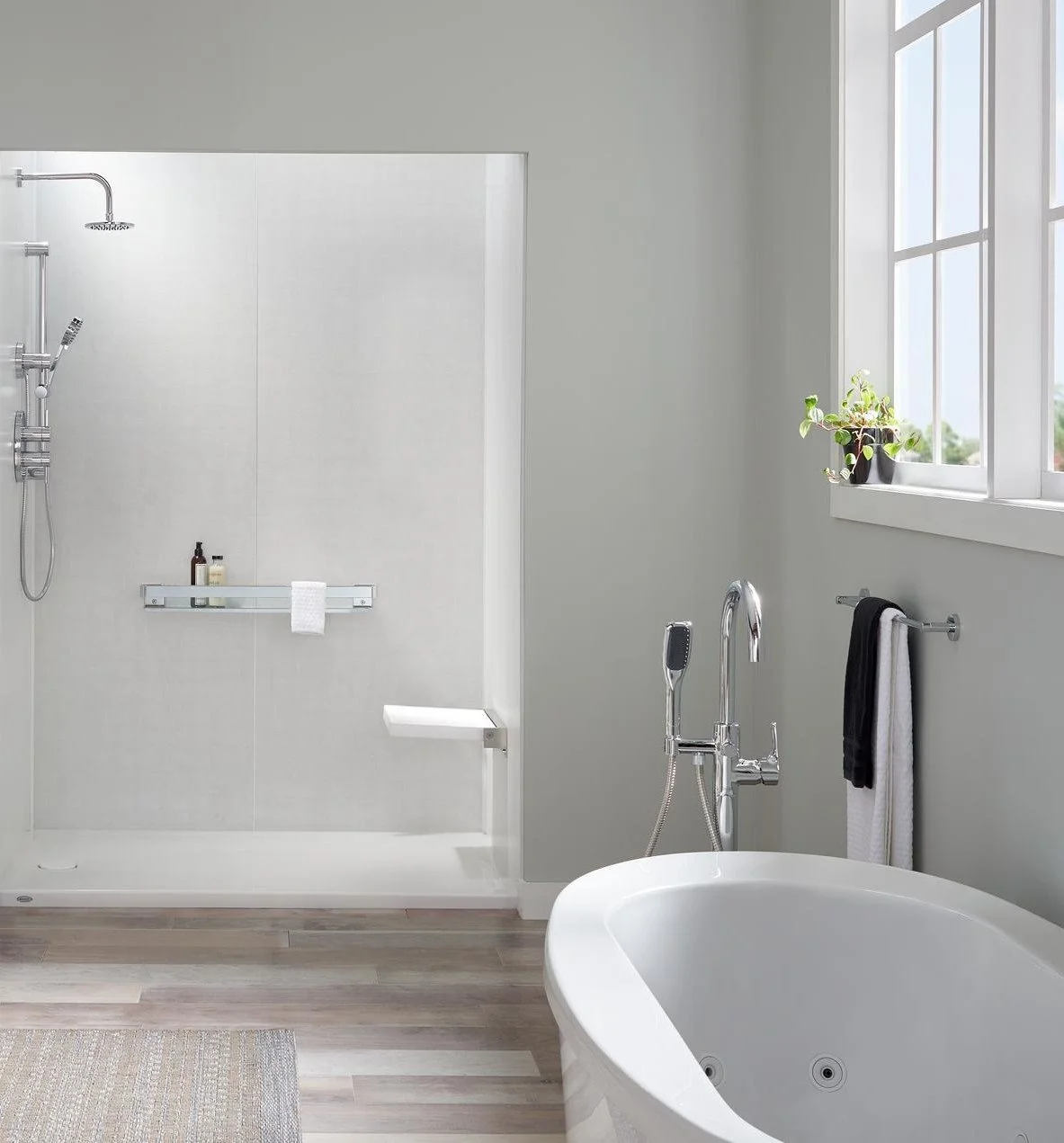Modern bathroom with a white bathtub, a shower area with a handheld showerhead, a small white shelf with toiletries, and a window with a potted plant on the windowsill.