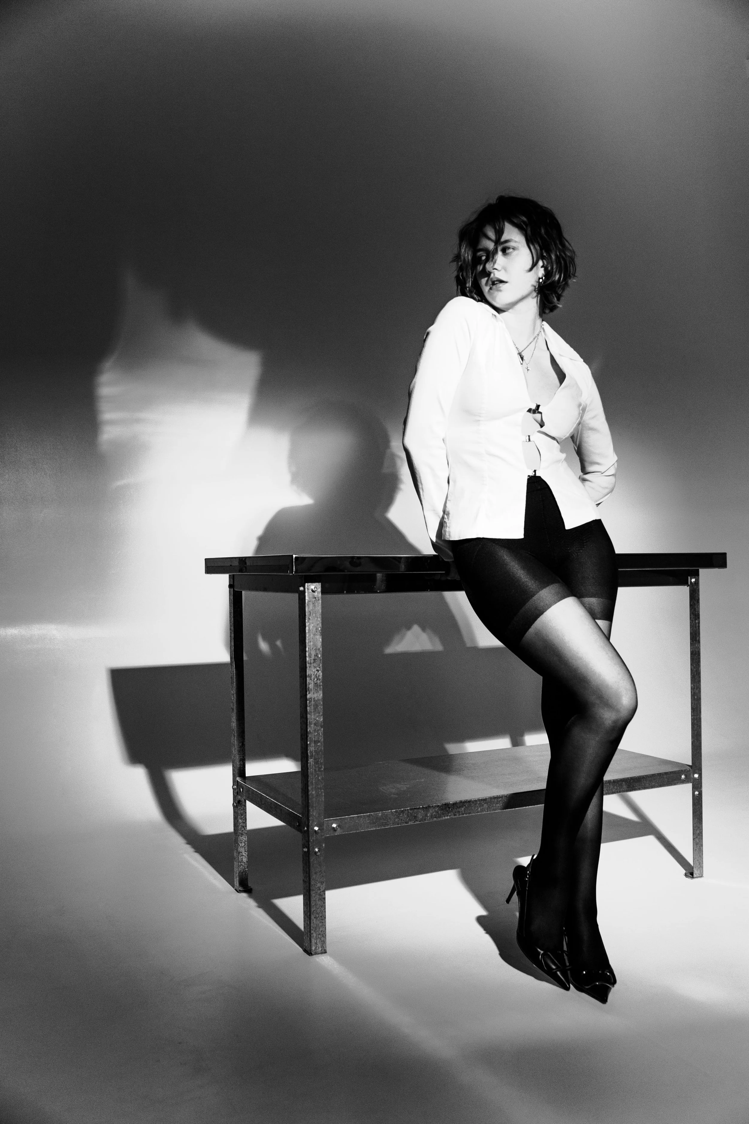 Woman in a white blouse and stockings sitting on a table, black and white photo.