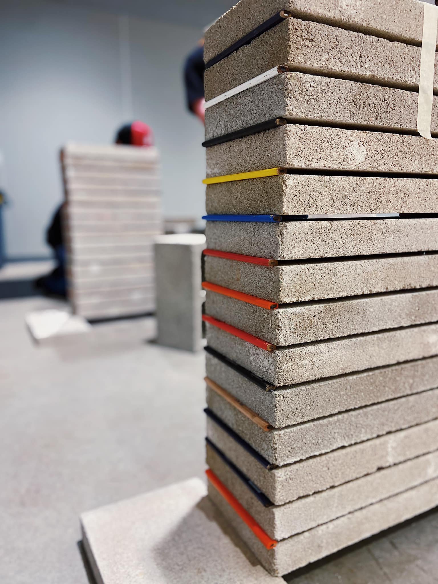 A vertical stack of rectangular concrete slabs with colored edges, including red, yellow, blue, and orange, in an indoor setting.
