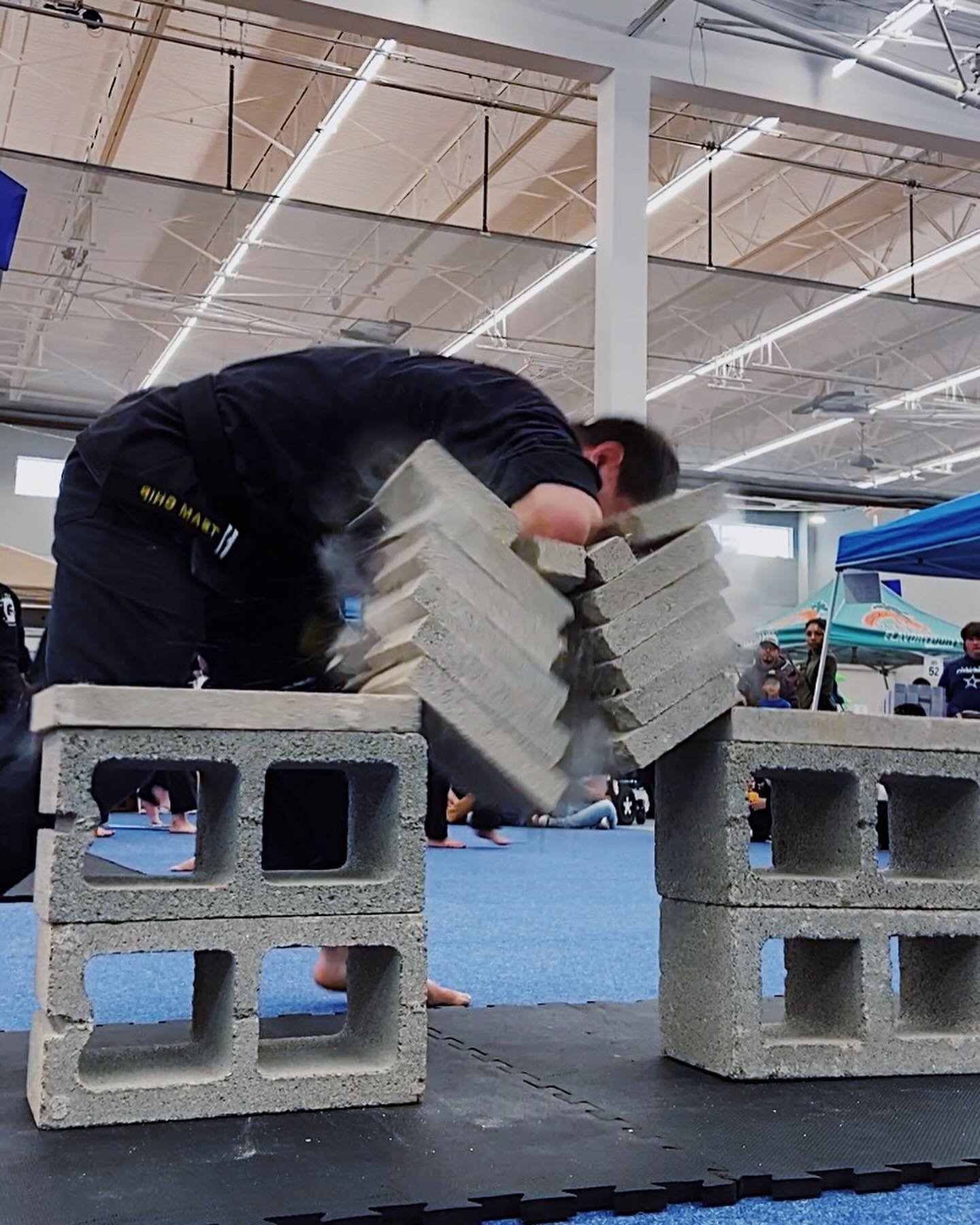 Person performing a martial arts brick-breaking demonstration, striking a stack of concrete blocks indoors.