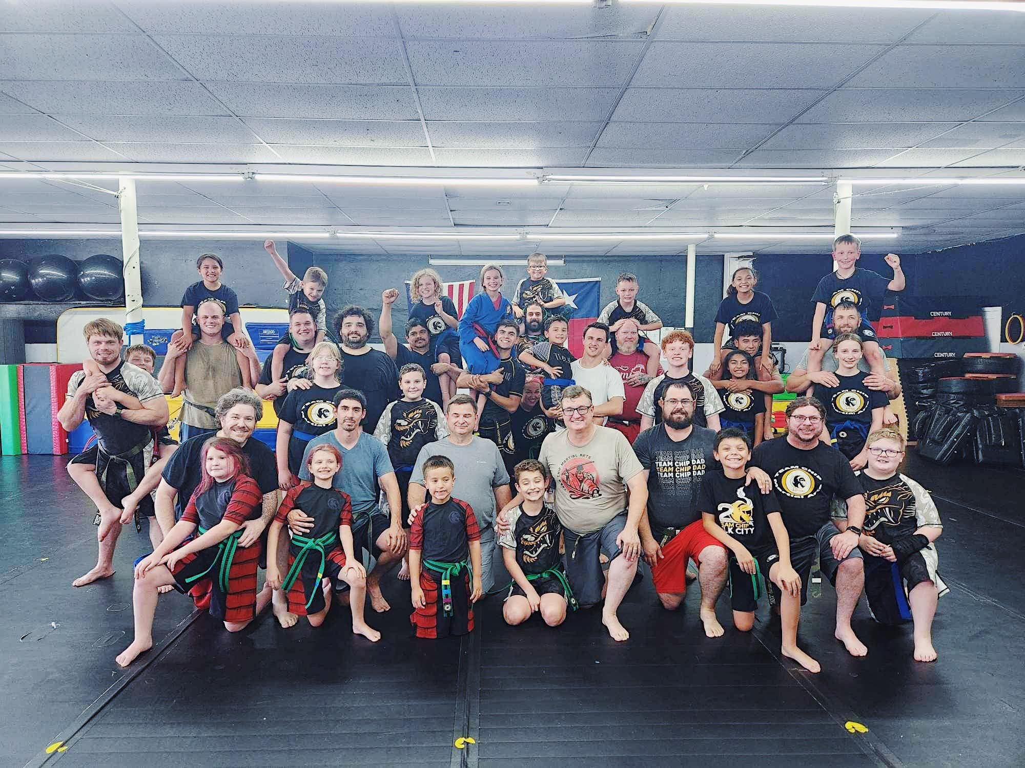 Group martial arts class with people of various ages posing in a dojo.