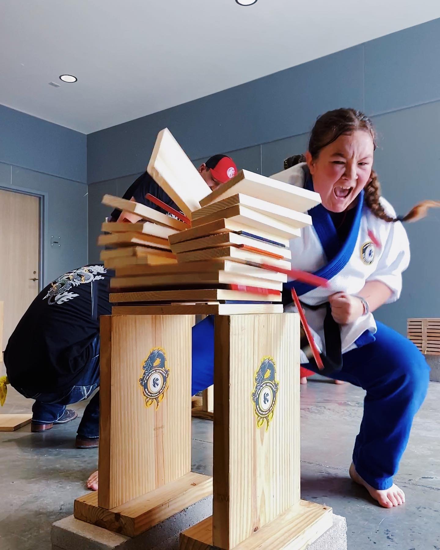 Martial artist breaking wood boards with a hand strike in a dojo setting, showing intense focus and power.