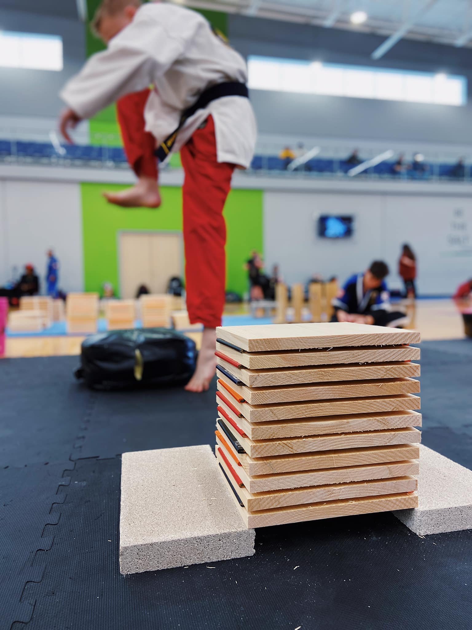 Martial artist in motion preparing to break stacked wooden boards during a competition in a gymnasium.